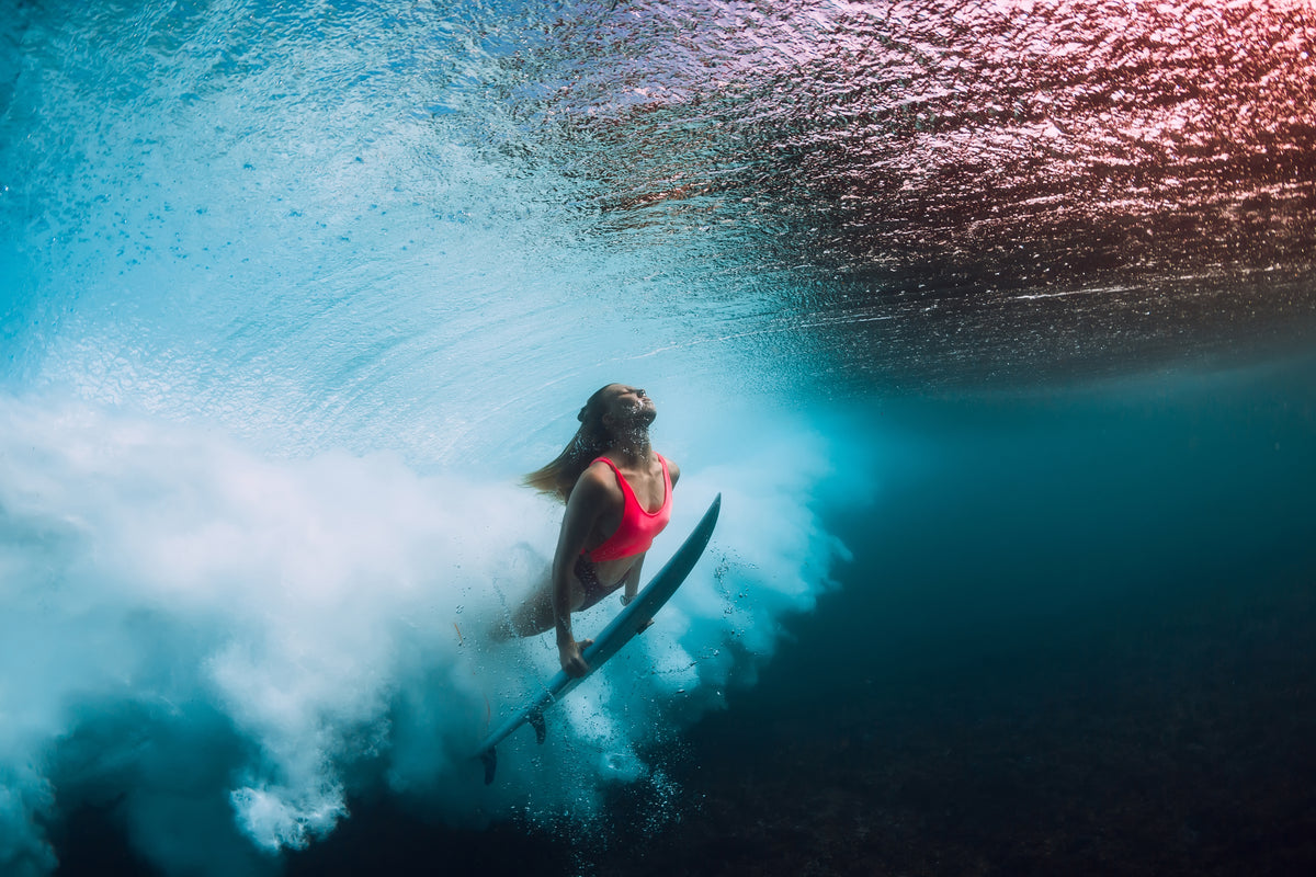 Surfer duck-diving under a breaking wave with her board
